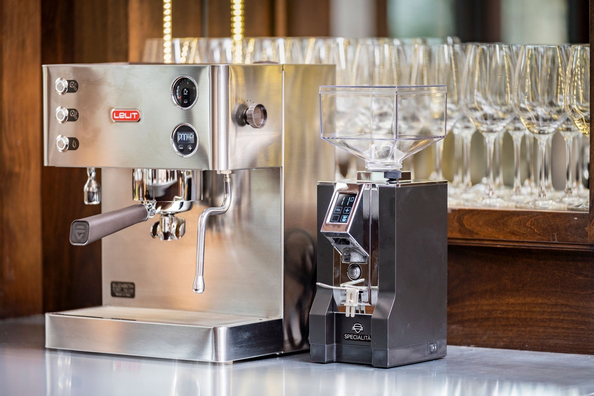Stainless Lelit espresso machine with a portafilter on a counter and a grinder with a clear hopper in the background