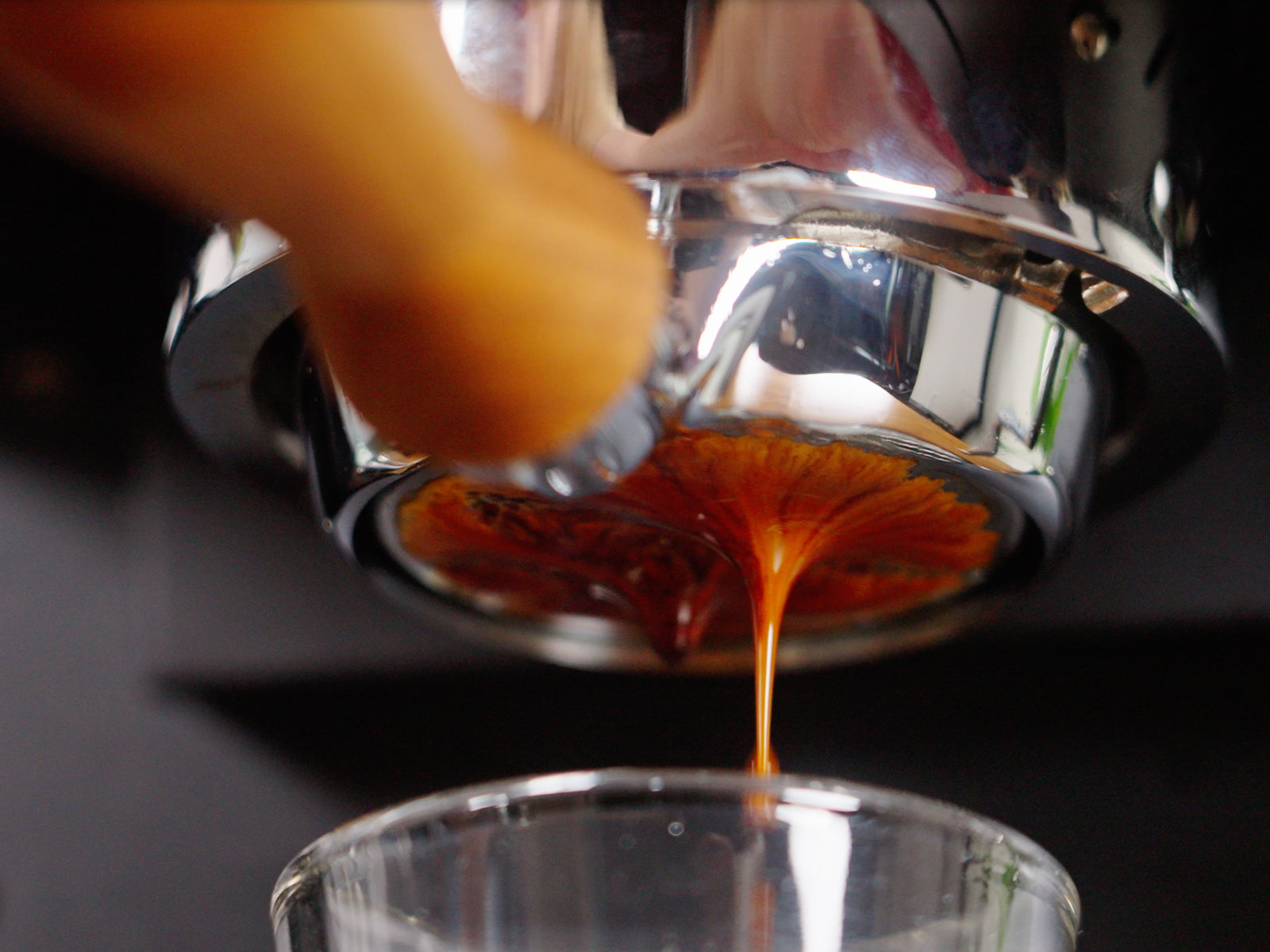 Espresso being pulled with crema streaming into a glass beneath a shiny portafilter