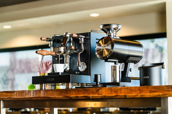 LUCCA M58 Sunto espresso machine pulling a shot next to a stainless steel Mazzer Philos grinder, lifestyle, by Clive Coffee