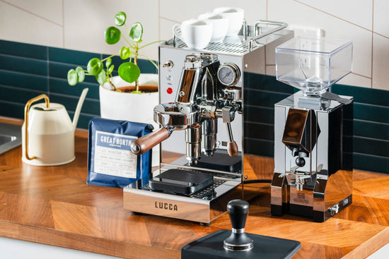 Shiny espresso machine with white cups on top and a Great North Coffee bag on a wooden counter