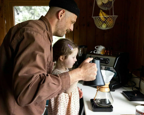 Father and daughter using a home espresso setup in a cozy kitchen.