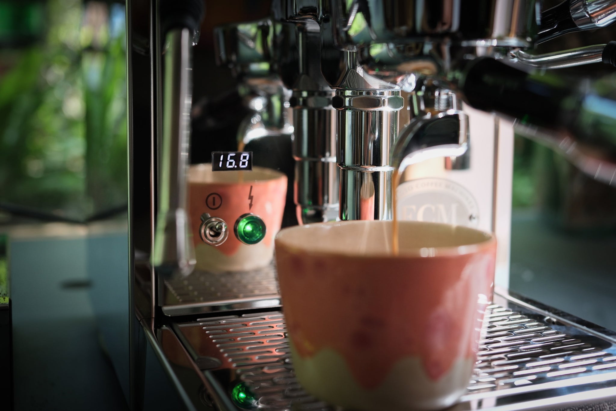 Shiny espresso machine with a pink ceramic cup under the group head and a digital display.