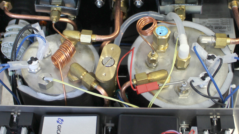 Close up of a commercial espresso machine internals showing copper tubes and fittings.