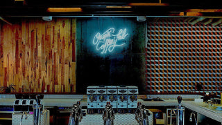 Cafe interior with a row of espresso machines along a tiled counter and a neon coffee sign