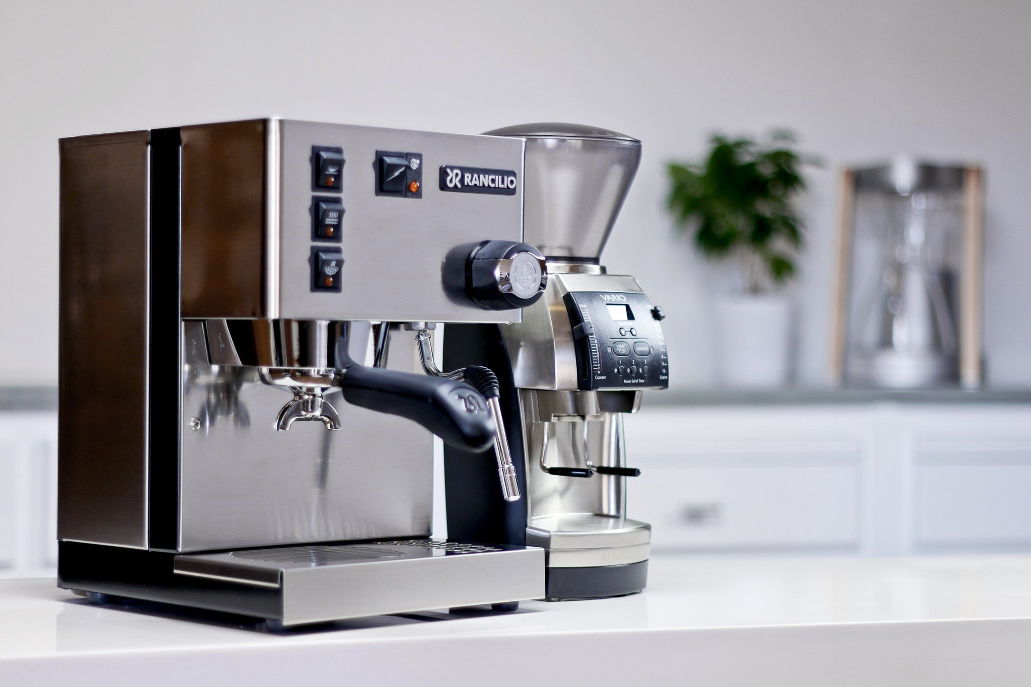 Rancilio espresso machine paired with a Baratza Vario grinder on a bright countertop with a plant in the background