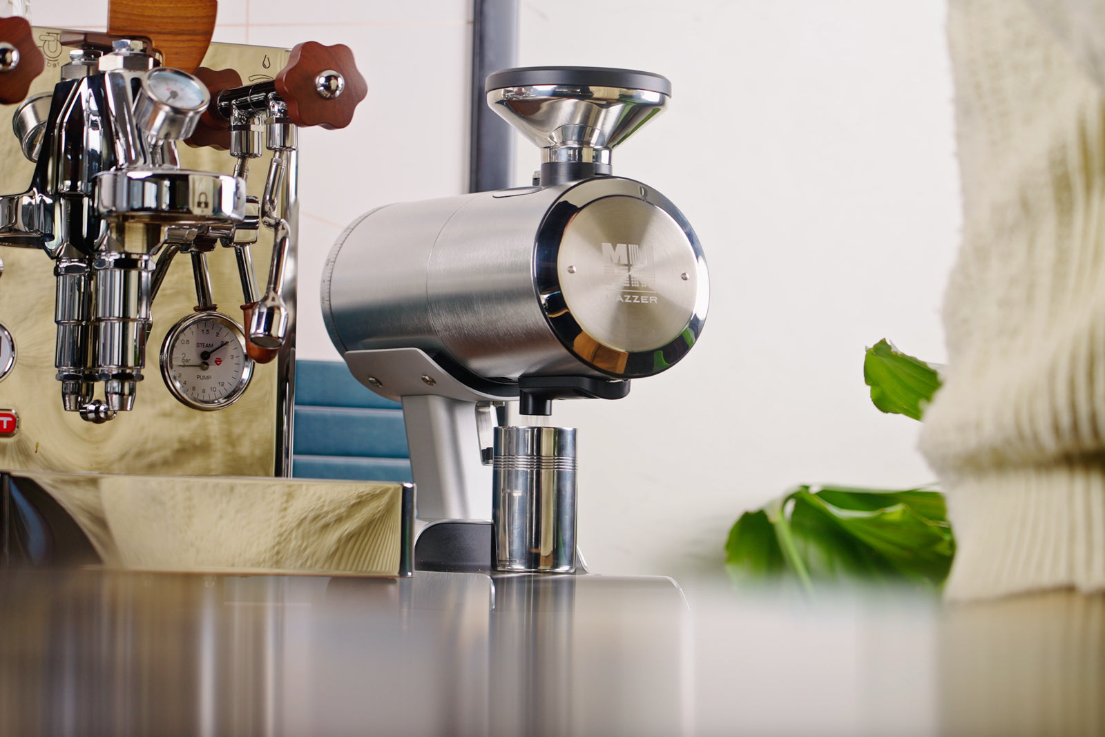 Close up of a polished espresso grinder beside a chrome espresso machine in a cafe.