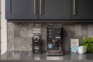 Sleek black espresso station in a kitchen with an Olympia Coffee bag and a white mug on the counter.