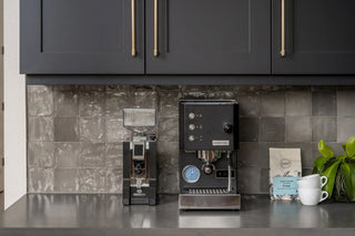 Modern espresso station with a black espresso machine and a grinder beneath dark upper cabinets