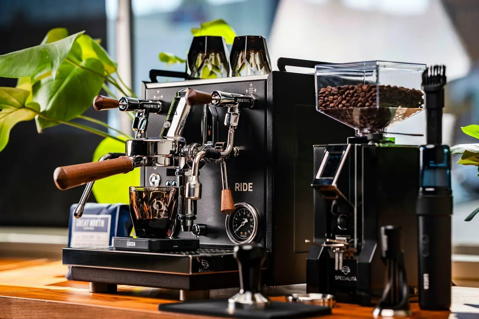 Dual group head espresso machine with wooden portafilter handles and a bean hopper on a counter.