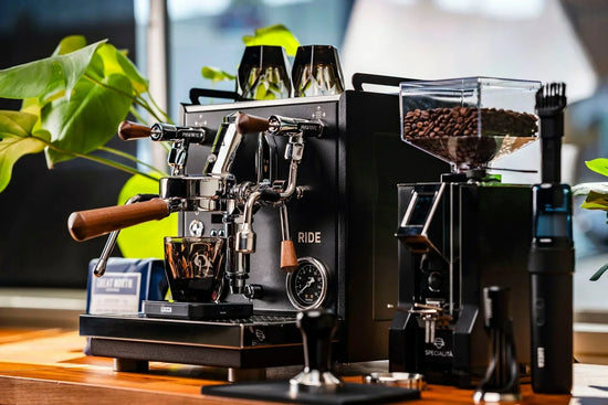 Dual group head espresso machine with wooden portafilter handles and a bean hopper on a counter.