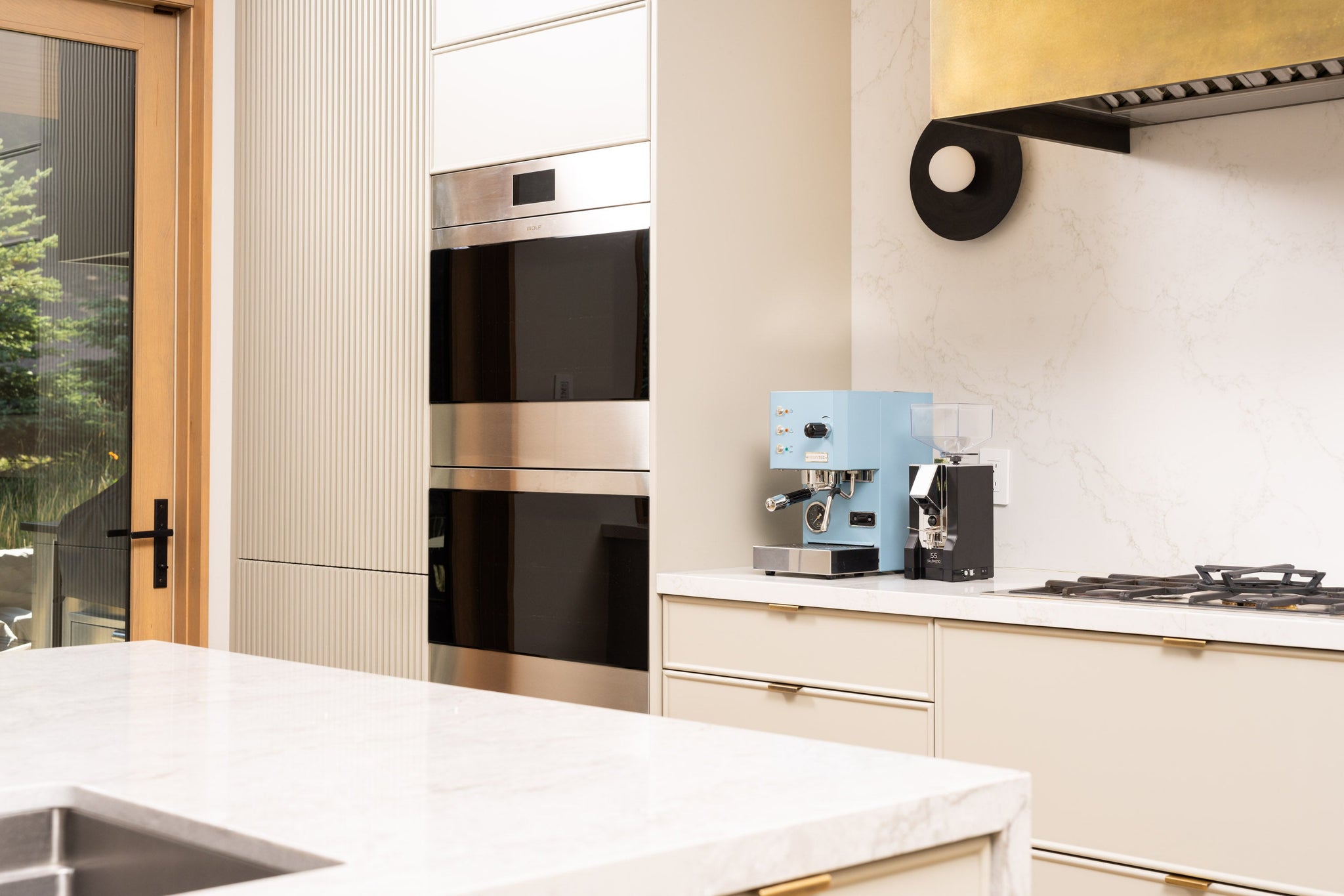 Blue compact home espresso machine on a white kitchen counter beside a built in stainless steel oven