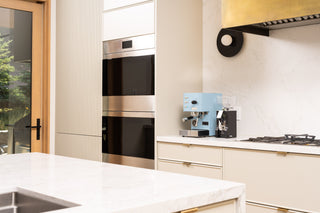 Blue compact home espresso machine on a white kitchen counter beside a built in stainless steel oven