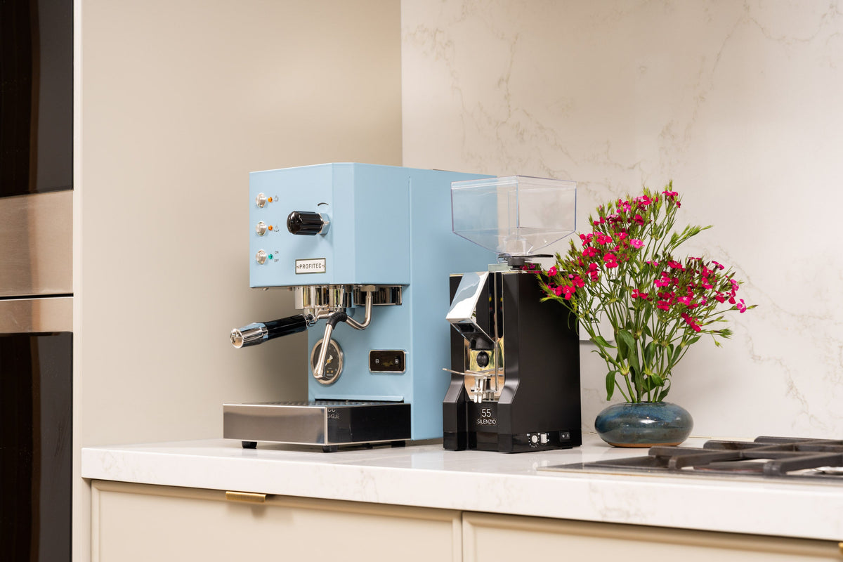 Blue Eureka Mignon Silenzio 55 grinder on a white kitchen counter beside a vase of pink flowers