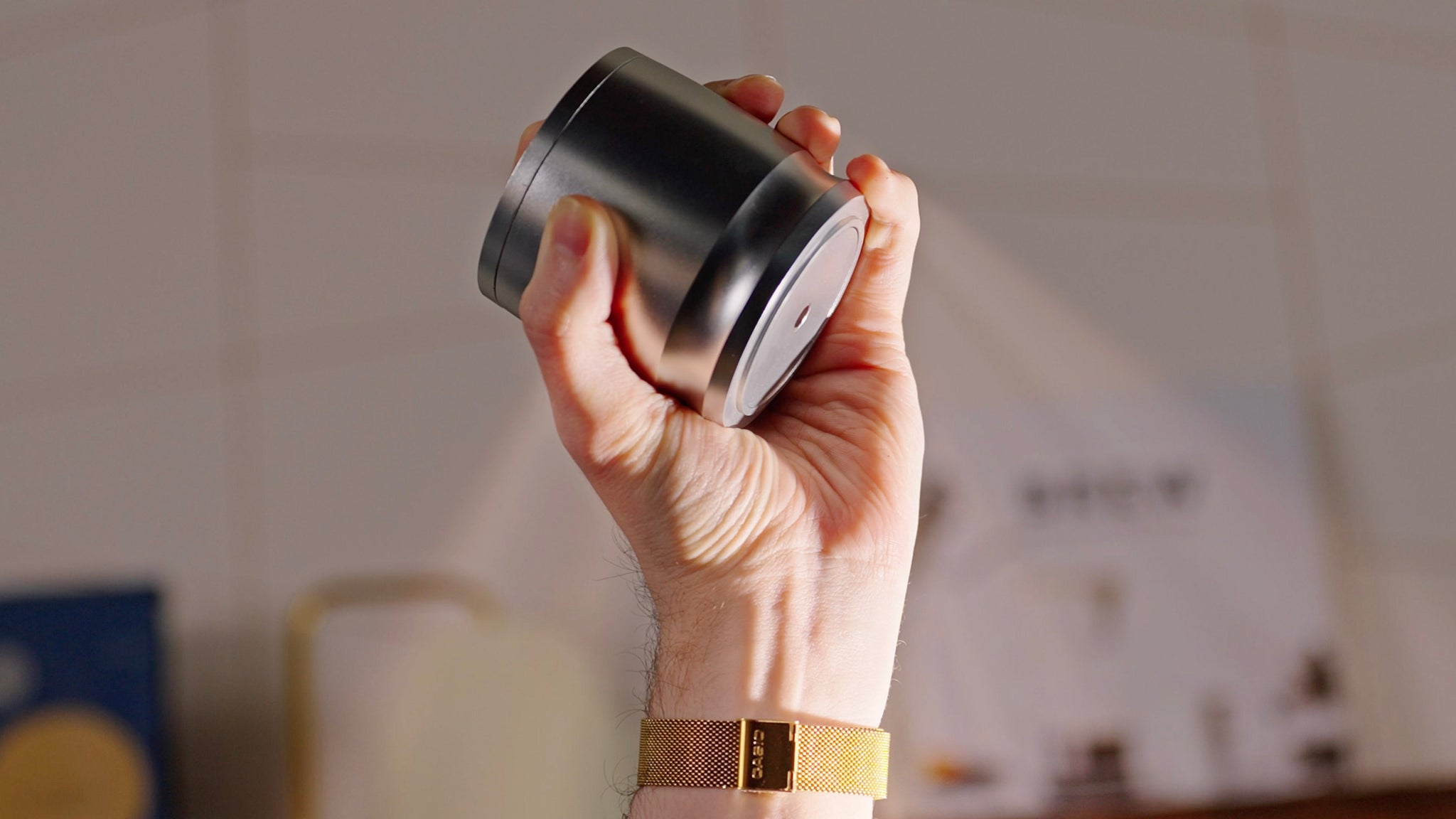 Hand gripping a cylindrical metal espresso puck screen tool with a flat base.