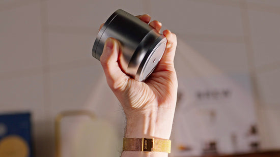 Hand gripping a cylindrical metal espresso puck screen tool with a flat base.