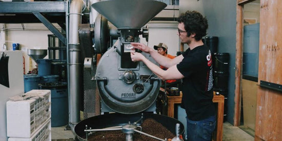 Technician adjusts a large Probat coffee roasting machine in a busy roastery.