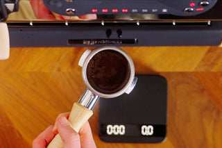 Overhead view of a hand holding a metal espresso portafilter filled with dark damp grounds