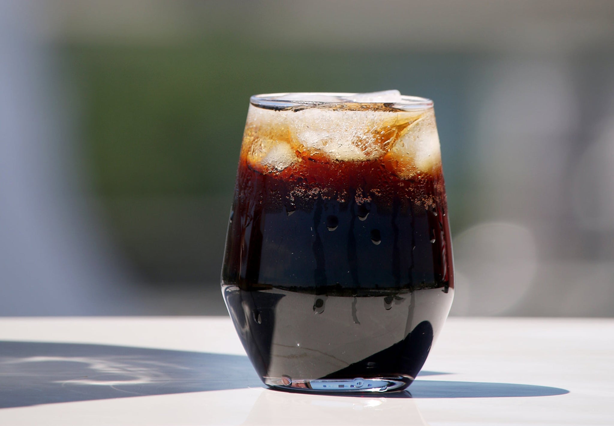 Iced coffee in a glass on a bright outdoor table with condensation and blurred background