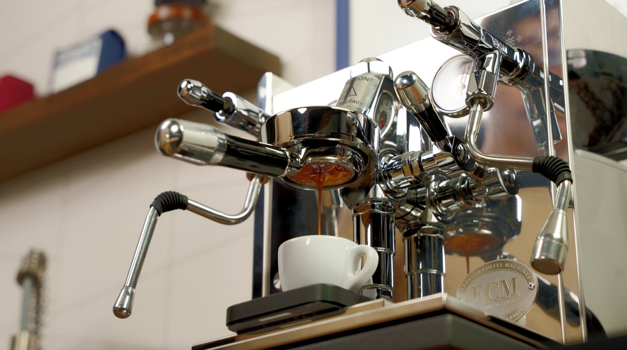 Close up of a chrome espresso machine with a portafilter and espresso dripping into a white cup