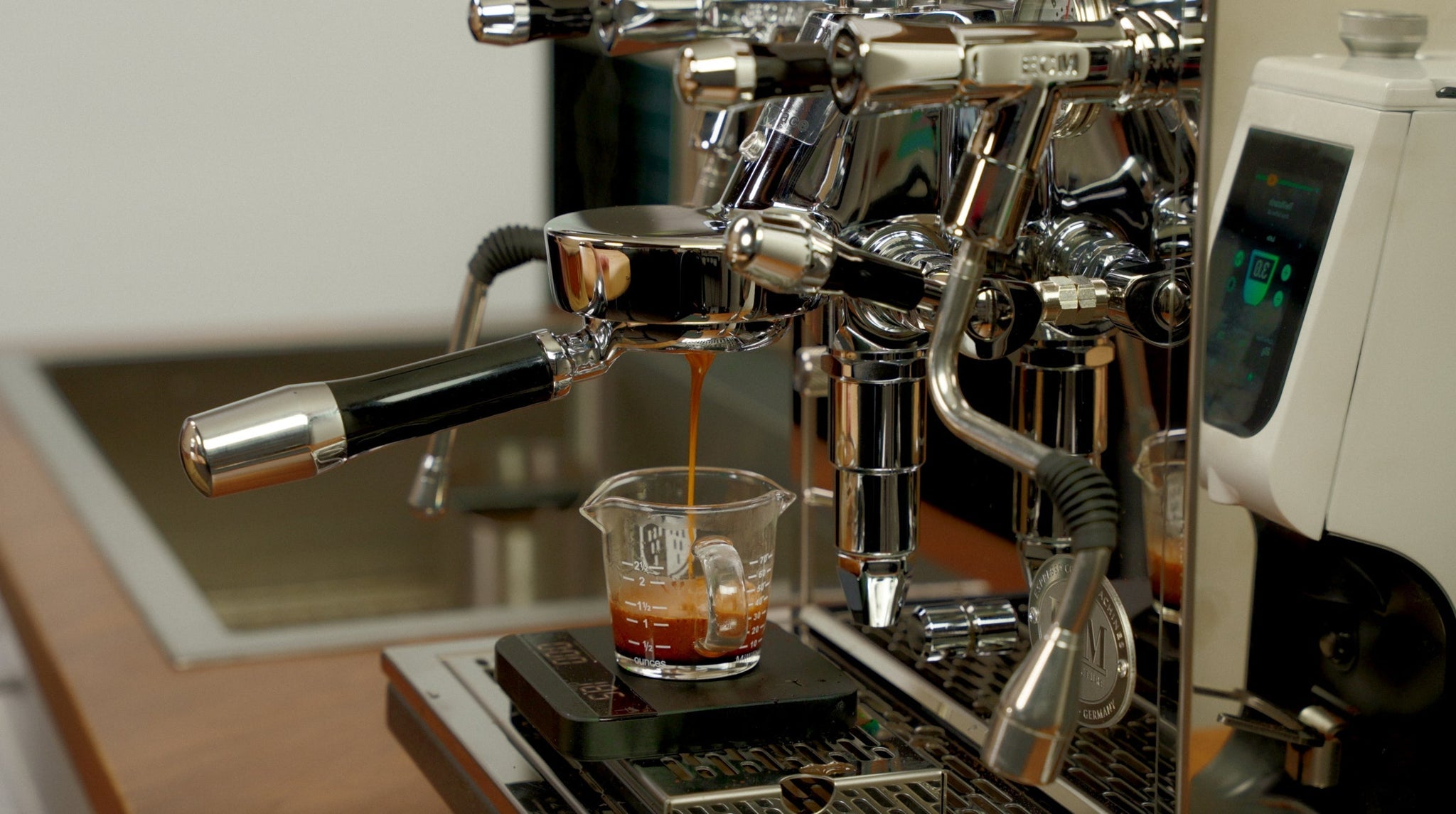 Espresso dripping into a glass measuring cup from a portafilter with crema visible