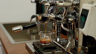Espresso dripping into a glass measuring cup from a portafilter with crema visible