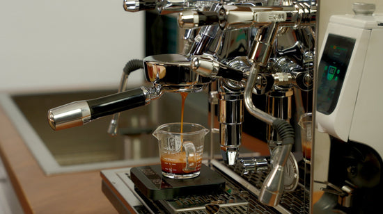 Espresso dripping into a glass measuring cup from a portafilter with crema visible