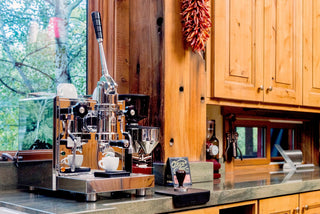 Classic manual lever espresso machine on a wooden counter with a tall chrome lever and black handle.