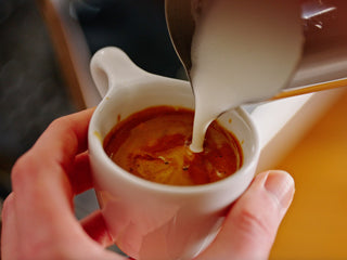 Foaming milk being poured into a small white espresso cup.