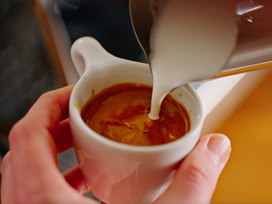 Foaming milk being poured into a small white espresso cup.