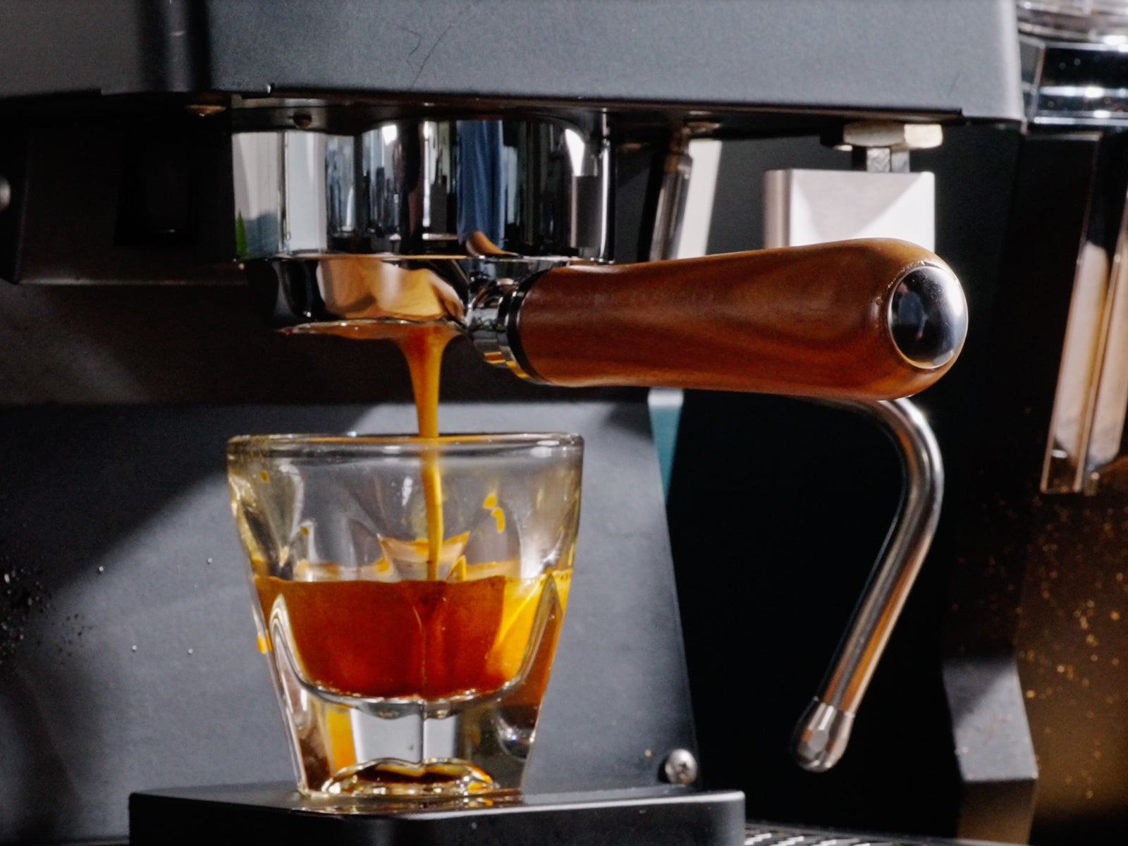 Espresso flows from a portafilter into a glass beneath a metallic coffee machine.