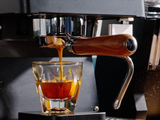 Espresso flows from a portafilter into a glass beneath a metallic coffee machine.