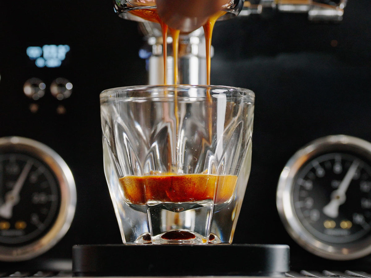Espresso machine pouring a shot into a clear glass with rich crema forming at the bottom.