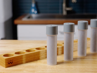 Row of light grey capped tubes in a wooden rack on a kitchen counter.
