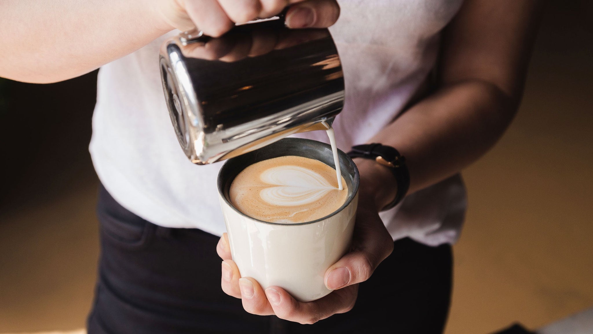 Close up of latte art as milk is poured into espresso in a white cup.