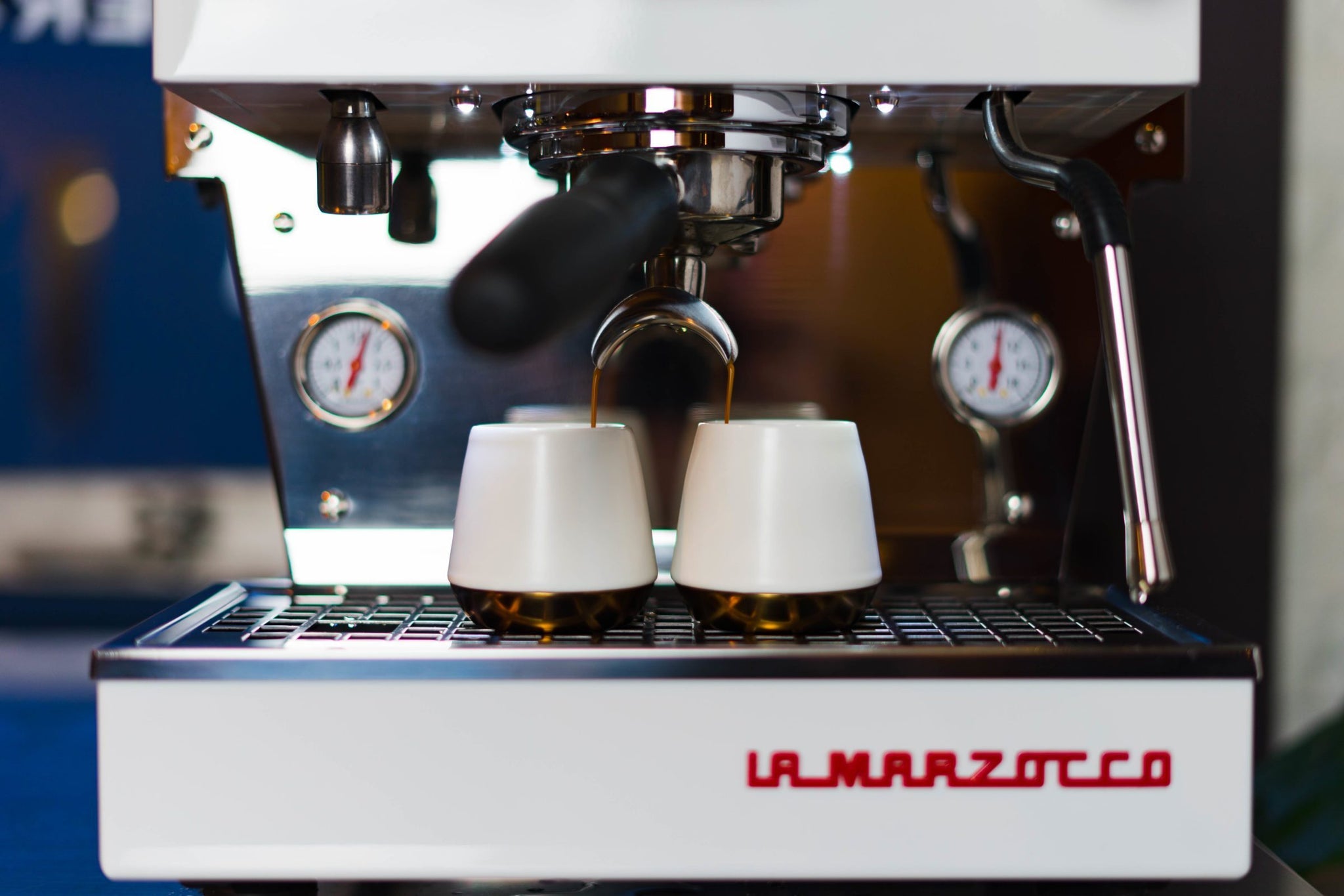 Dual spouts pour espresso into two white cups beneath a La Marzocco espresso machine.