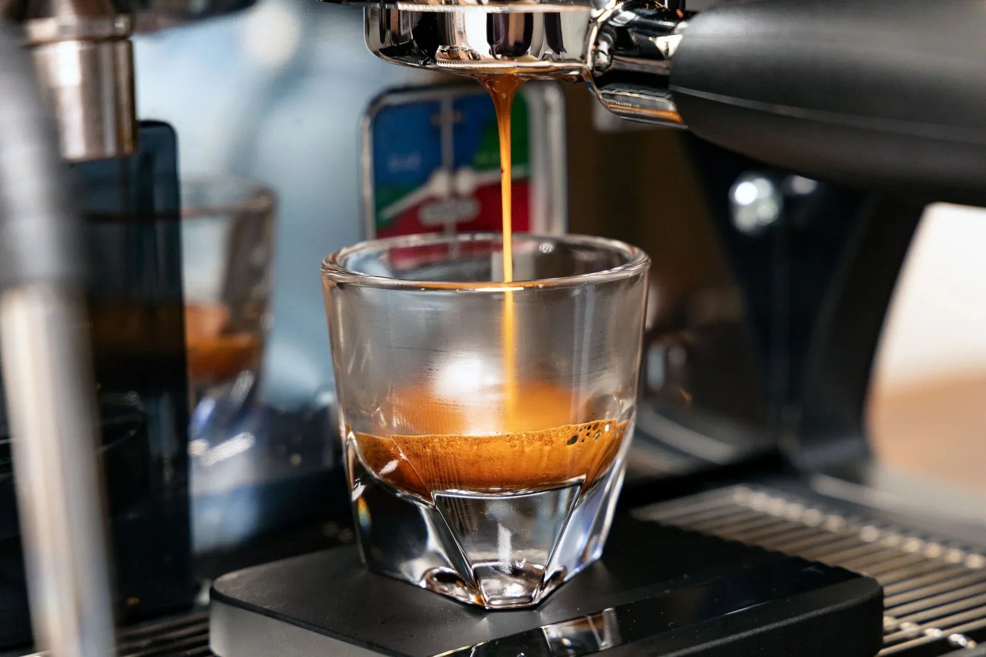 Espresso streams into a clear glass from a shiny espresso machine.