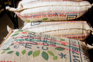 Stacked burlap coffee sacks with faded prints and green leaf patterns
