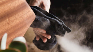 Hands wringing a dark cloth with steam rising in the background.