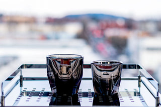 Two dark glass cups on a glass surface with a blurred cityscape background
