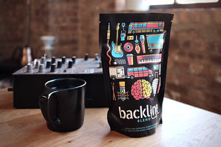 Backline Blend coffee bag on a wooden table with a black mug and a music mixer in a studio.