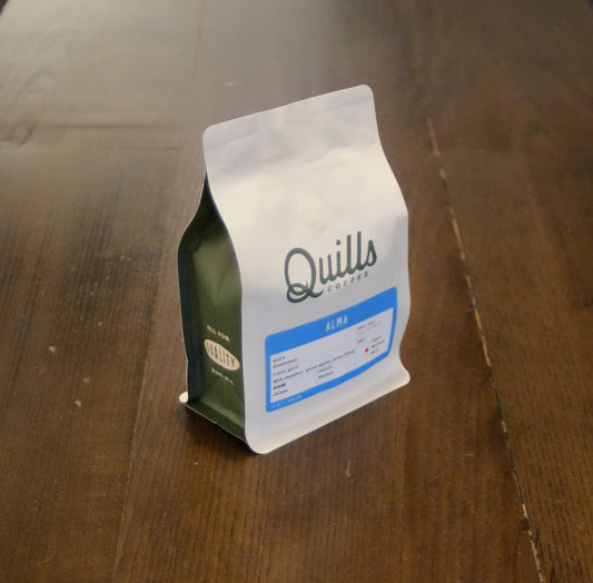 Close-up of a Quills Alma coffee label on a bottle resting on a wooden table