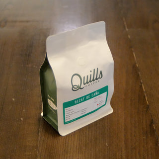 Close-up of Decaf de Cana bottle label from Quills Coffee on a wooden surface.