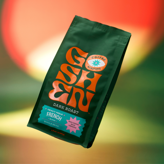 Heavy Feels French dark roast coffee bag held by white hands against a red background