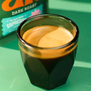 Close-up of coffee crema in a glass with the green bag and turquoise label in the blurred background.
