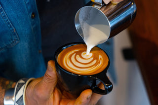 Barista pours steamed milk into a cup to form latte art during a home barista class