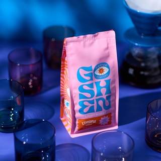 Pink Ethiopia Biruhi coffee bag shown under blue lighting beside glassware.