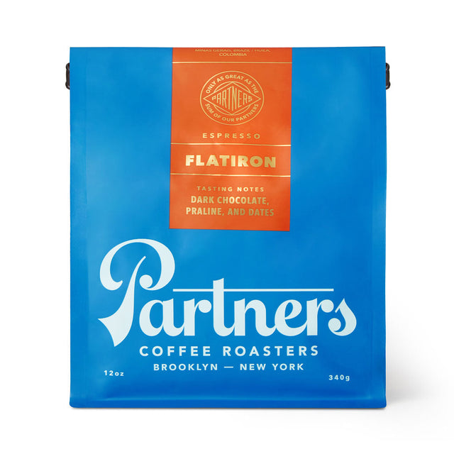 Bright blue Partners Coffee Flatiron espresso bag with orange label listing tasting notes dark chocolate praline and dates.
