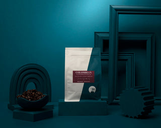 Parisi Colombian Decaf bag with a bowl of roasted coffee beans on a teal display.