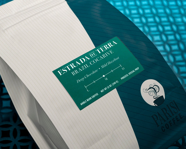 Estrada de Terra coffee packaging with teal label on a blue striped surface beside notebook pages.