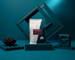 Nicaragua Jinotega coffee bag on a teal surface with a bowl of roasted coffee beans nearby.